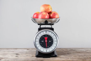 Mechanical kitchen scale with bowl of apples on wooden table against grey background