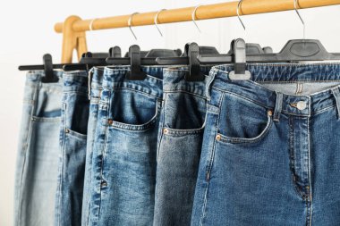 Many stylish jeans hanging from rack on white background, closeup