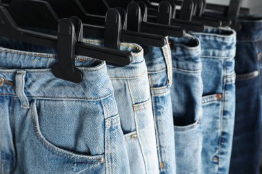 Many stylish jeans with hangers, closeup view