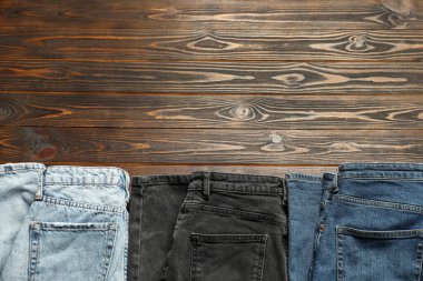 Different stylish jeans on wooden background, flat lay. Space for text