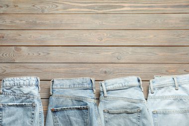 Different stylish jeans on wooden background, flat lay. Space for text