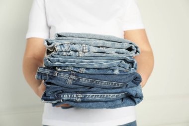 Kapalı alandaki aydınlık duvarın yanında farklı şık kot pantolonları olan kadın, yakın plan.