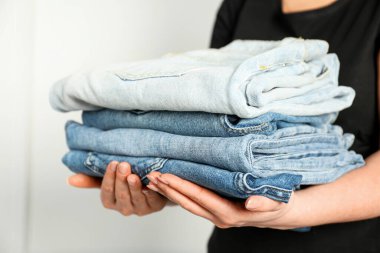 Kapalı alandaki aydınlık duvarın yanında farklı şık kot pantolonları olan kadın, yakın plan.