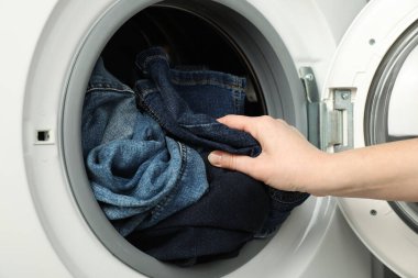 Kadın çamaşır makinesine kot pantolon koyuyor, yakın plan.