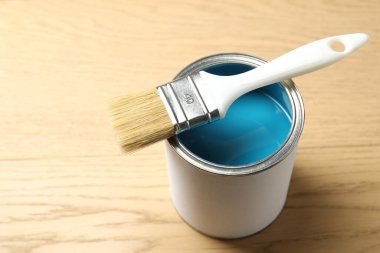 Can of light blue paint and brush on wooden background, closeup