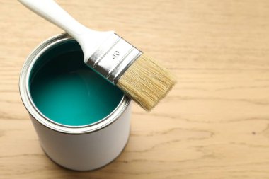 Can of turquoise paint and brush on wooden background, closeup. Space for text