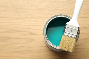 Can of turquoise paint and brush on wooden background, top view. Space for text