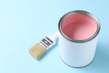 Can of pink paint and brush on light blue background, closeup