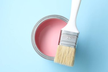 Can of pink paint and brush on light blue background, top view