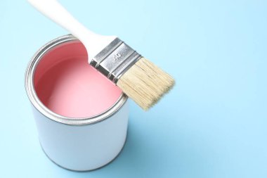 Can of pink paint and brush on light blue background, closeup. Space for text