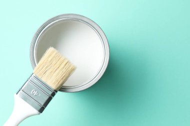 Can of white paint and brush on turquoise background, top view. Space for text