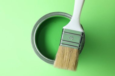 Can of bright paint and brush on light green background, top view