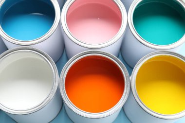 Cans of different paints on light blue background, closeup