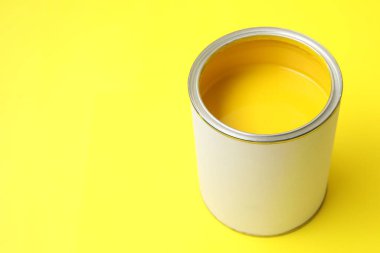 Can of bright paint on yellow background, closeup. Space for text