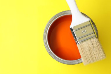 Can of orange paint and brush on yellow background, top view. Space for text