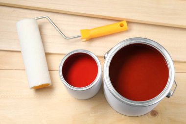 Cans of red paint, roller and planks on wooden table, above view