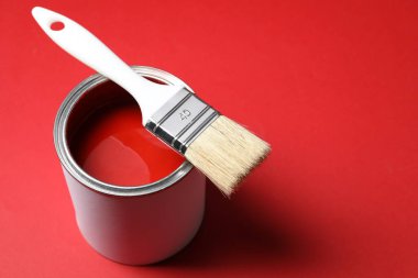 Can of bright paint and brush on red background, closeup. Space for text
