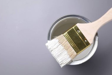 Can of white paint and brush on grey background, top view. Space for text