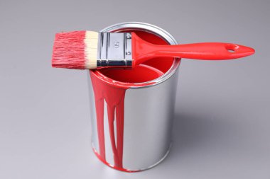 Can of red paint and brush on grey background, closeup