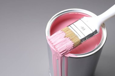 Can of pink paint and brush on grey background, closeup. Space for text