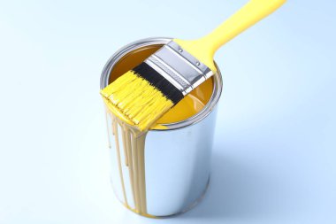 Can of yellow paint and brush on light background