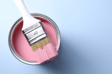 Can of pink paint and brush on light background, top view. Space for text