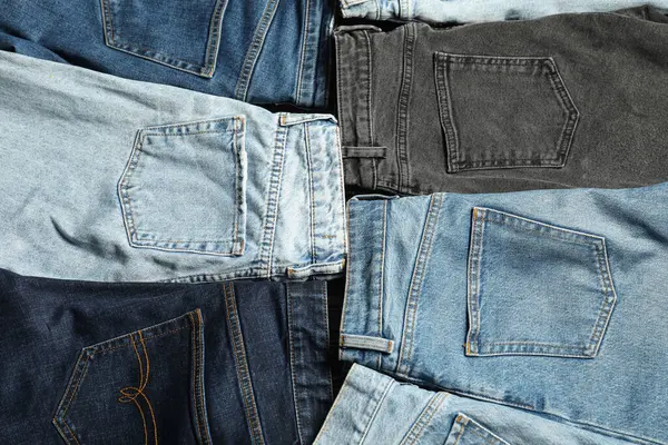 Different stylish jeans as background, top view
