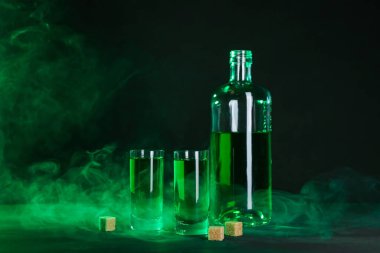 Absinthe shot bardakları, şişe ve esmer şeker siyah arka planda dumanlı