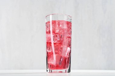 Sweet soda water with ice cubes in glass on white table, closeup
