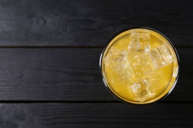 Sweet soda water with ice cubes in glass on black wooden table, top view. Space for text