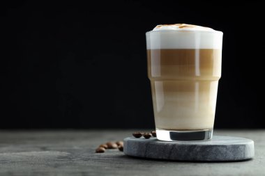 Tasty latte macchiato in glass and coffee beans on grey table, closeup. Space for text