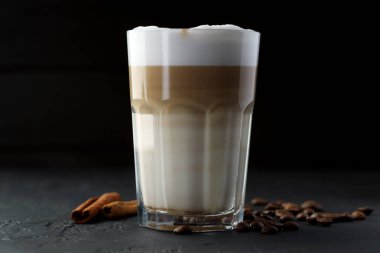 Bardakta latte macchiato, siyah masada kahve çekirdekleri ve tarçın, yakın plan.
