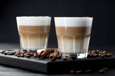 Bardakta latte macchiato, kahve çekirdekleri ve siyah ahşap masada tarçın, yakın plan.