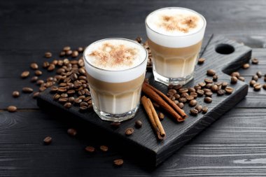 Bardakta latte macchiato, kahve çekirdekleri ve siyah ahşap masada tarçın, yakın plan.