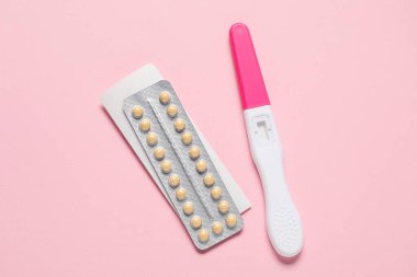 Blister of oral contraceptive pills and pregnancy test on pink background, flat lay