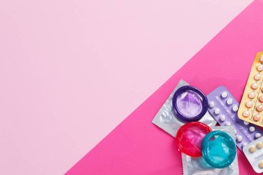 Pembe arka planda doğum kontrol hapı ve prezervatif kabarcıkları var. Metin için boşluk