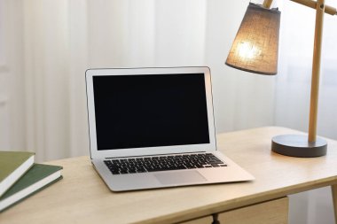 Comfortable workplace with modern laptop and lamp on wooden desk in home office