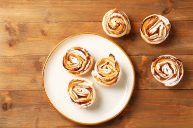 Tasty apple roses with powdered sugar on wooden table, flat lay