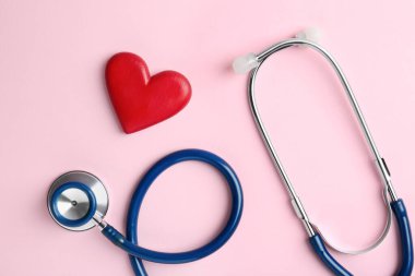 Kardiyoloji. Stetoskop ve soluk pembe arka planda kırmızı dekoratif kalp düz yatıyordu.