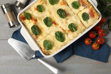 Delicious spinach lasagne in baking dish served on grey wooden table, flat lay