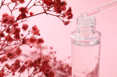 Pipetten şişeye serum damlıyor ve çingene çiçekleri pembe arka planda, yakın plan