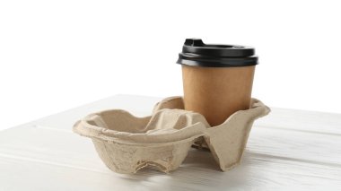 Paper coffee cup in cardboard holder on white wooden table. Space for text