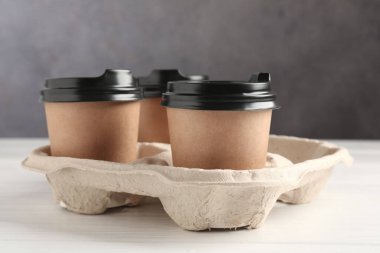 Kağıt kahve bardakları beyaz ahşap masadaki karton tutacakta, yakın plan.