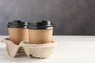 Paper coffee cups in cardboard holder on white wooden table, closeup. Space for text