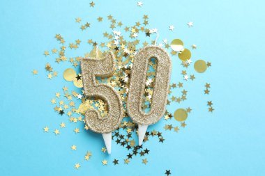 50th birthday. Number shaped candles and confetti on light blue background, flat lay