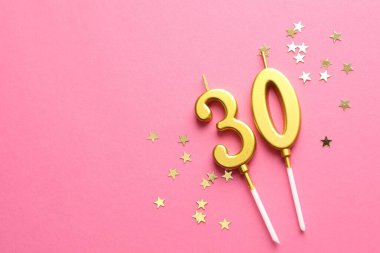 30th birthday. Number shaped candles and confetti on pink background, flat lay. Space for text