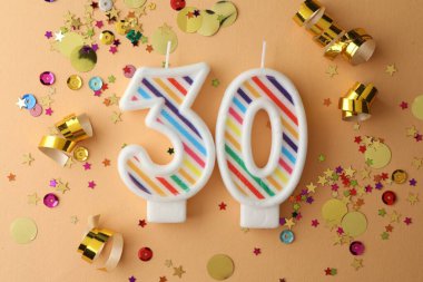 30th birthday. Number shaped candles and confetti on beige background, flat lay