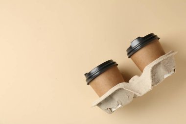 Paper coffee cups in cardboard holder on beige background, top view. Space for text