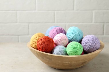 Balls of colorful yarn in bowl on light grey table, closeup
