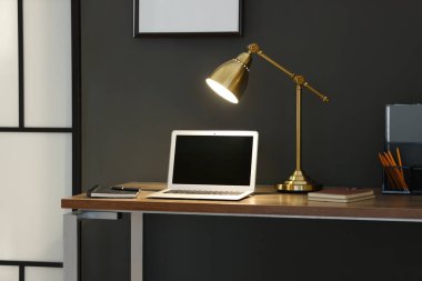 Home office. Comfortable workplace with laptop and lamp on wooden desk indoors